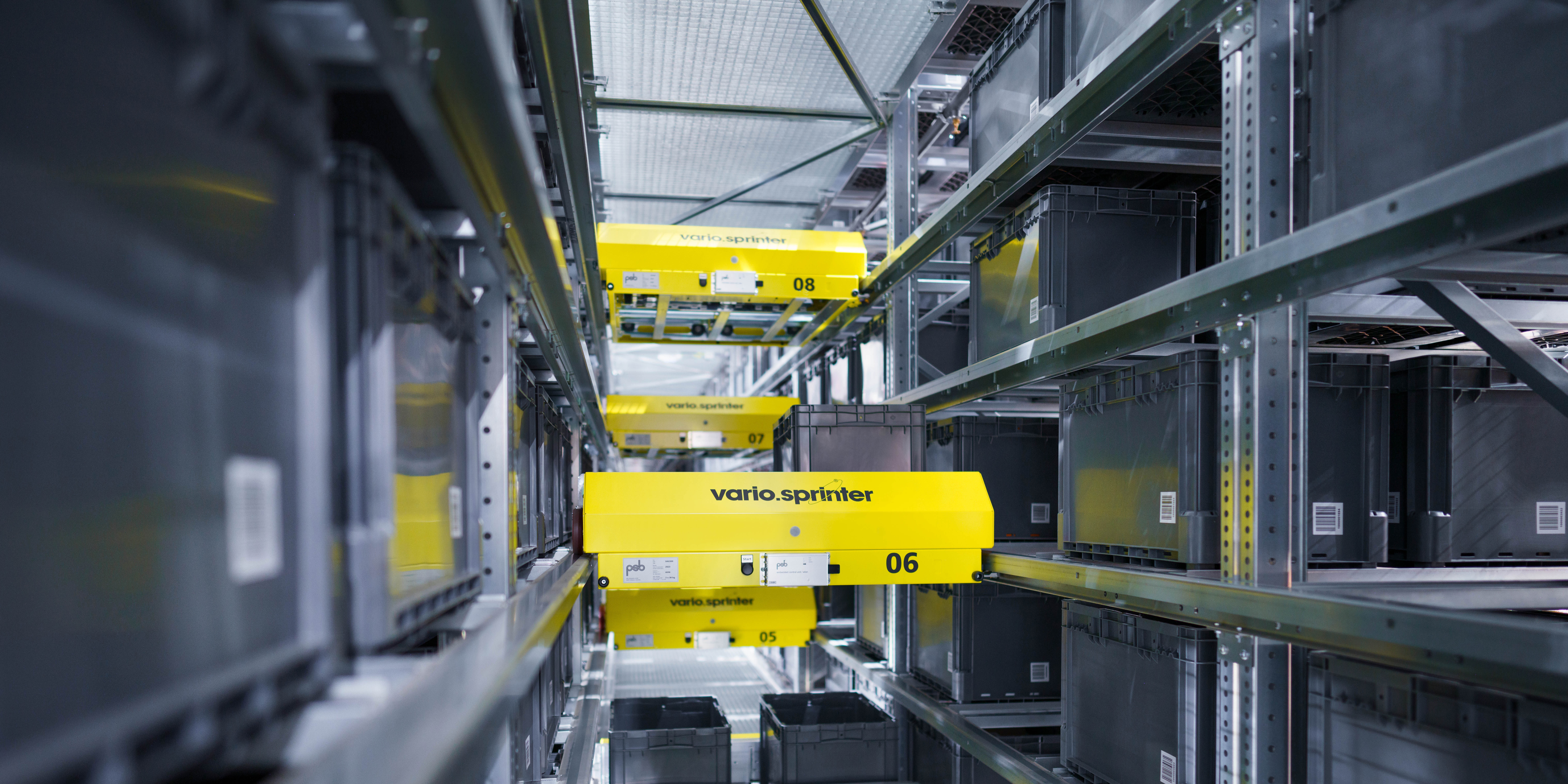 Zwei gelbe vario.sprinter Shuttles fahren zwischen dichten Regalen in einem microstore Lagersystem